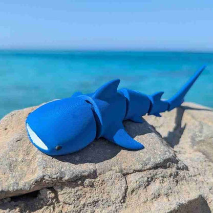 Blue shark-shaped toy on a rock with ocean in the background