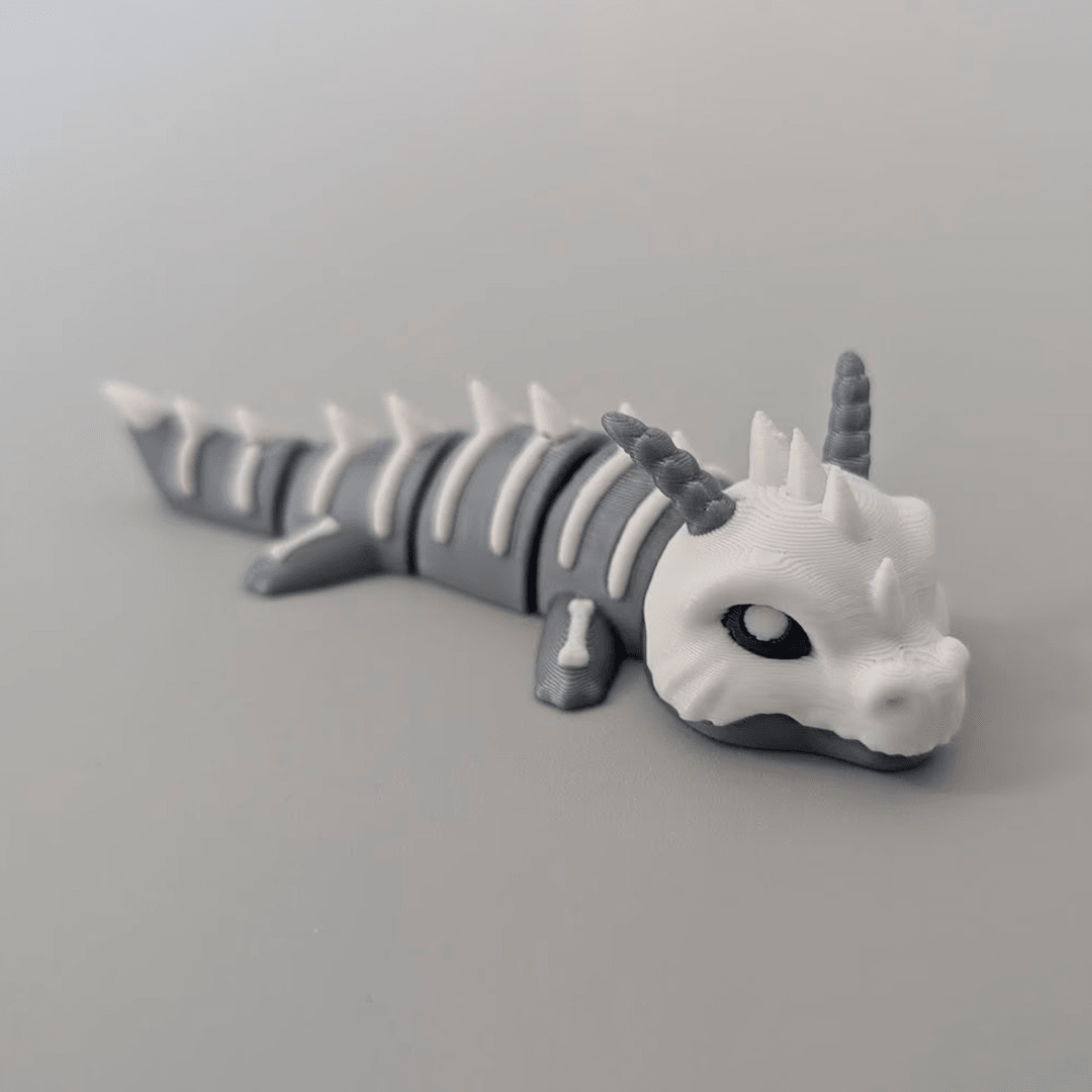 3D-printed Bone Dragon articulated flexi keychain in bone white, front view posed standing — 864 ToyLabs
Bone Dragon flexi keychain held in hand showing scale and skeletal detail — 864 ToyLabs